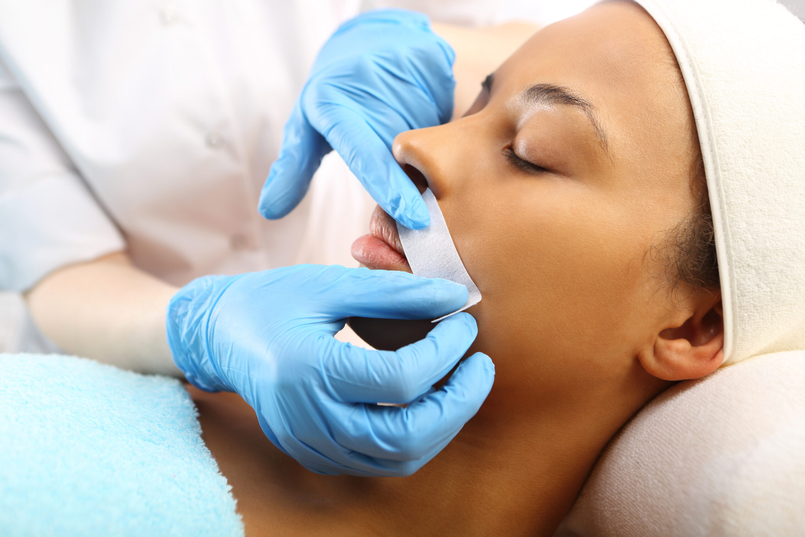 A skincare professional applies a facial wax strip to a client's upper lip